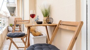A small balcony with wooden furniture, a glass of red wine, and a potted plant.