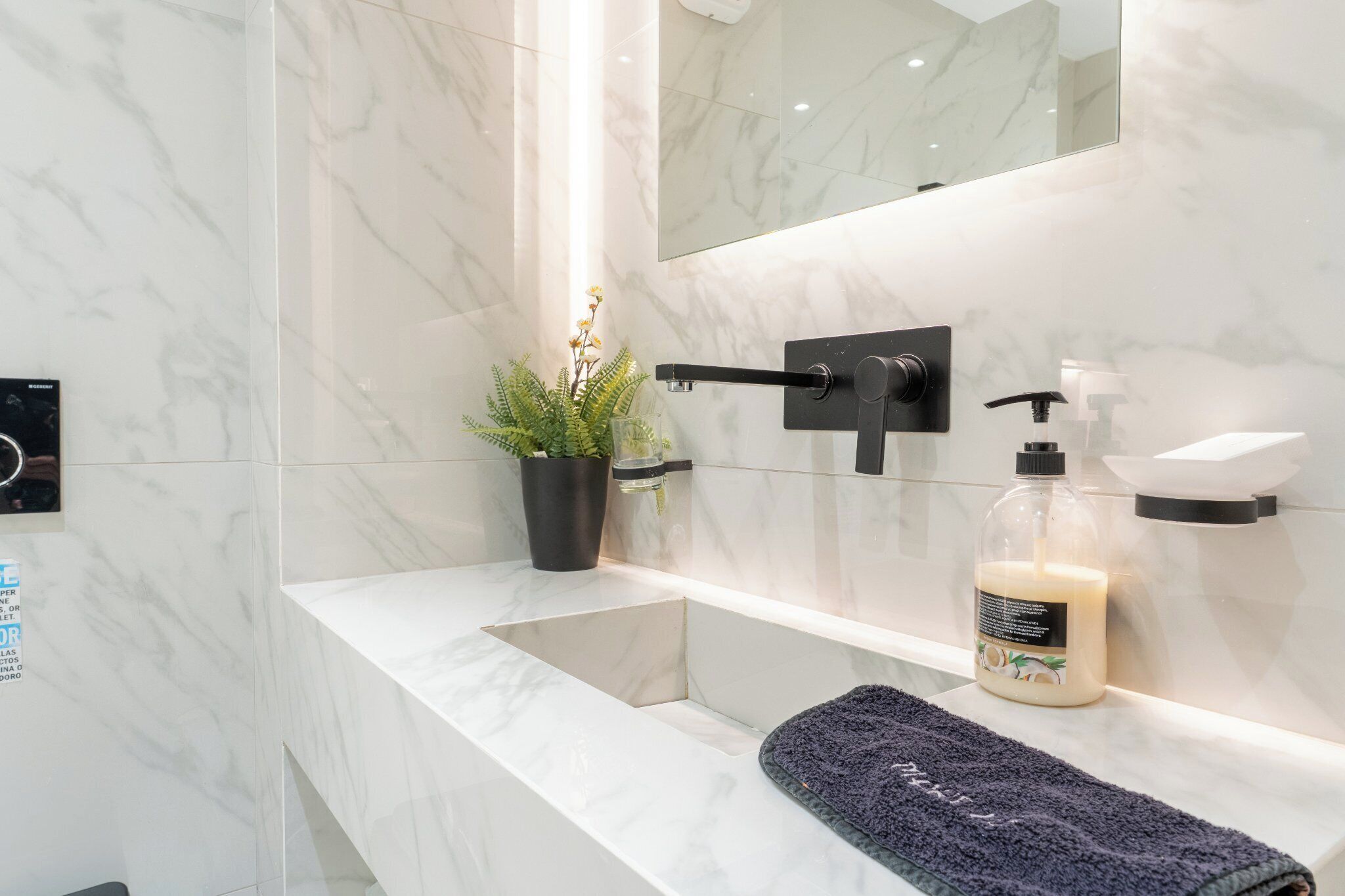 A modern bathroom with a marble sink, a black towel, a potted plant, and a hand soap dispenser.