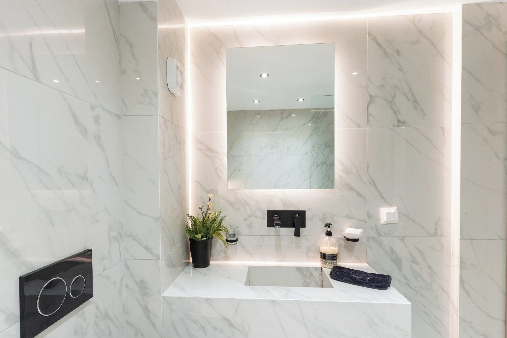 A modern bathroom with a marble vanity, a large mirror, and a potted plant.