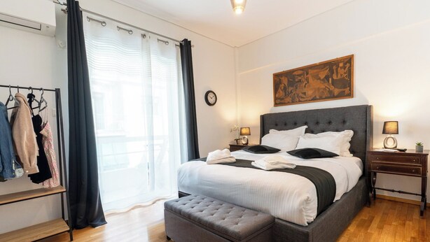 A neatly arranged bedroom with a large bed, a side table, a clock, and a painting on the wall.