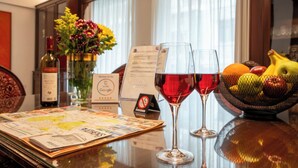 A table with two wine glasses, a bottle of wine, a vase with flowers, a fruit bowl, and a menu.