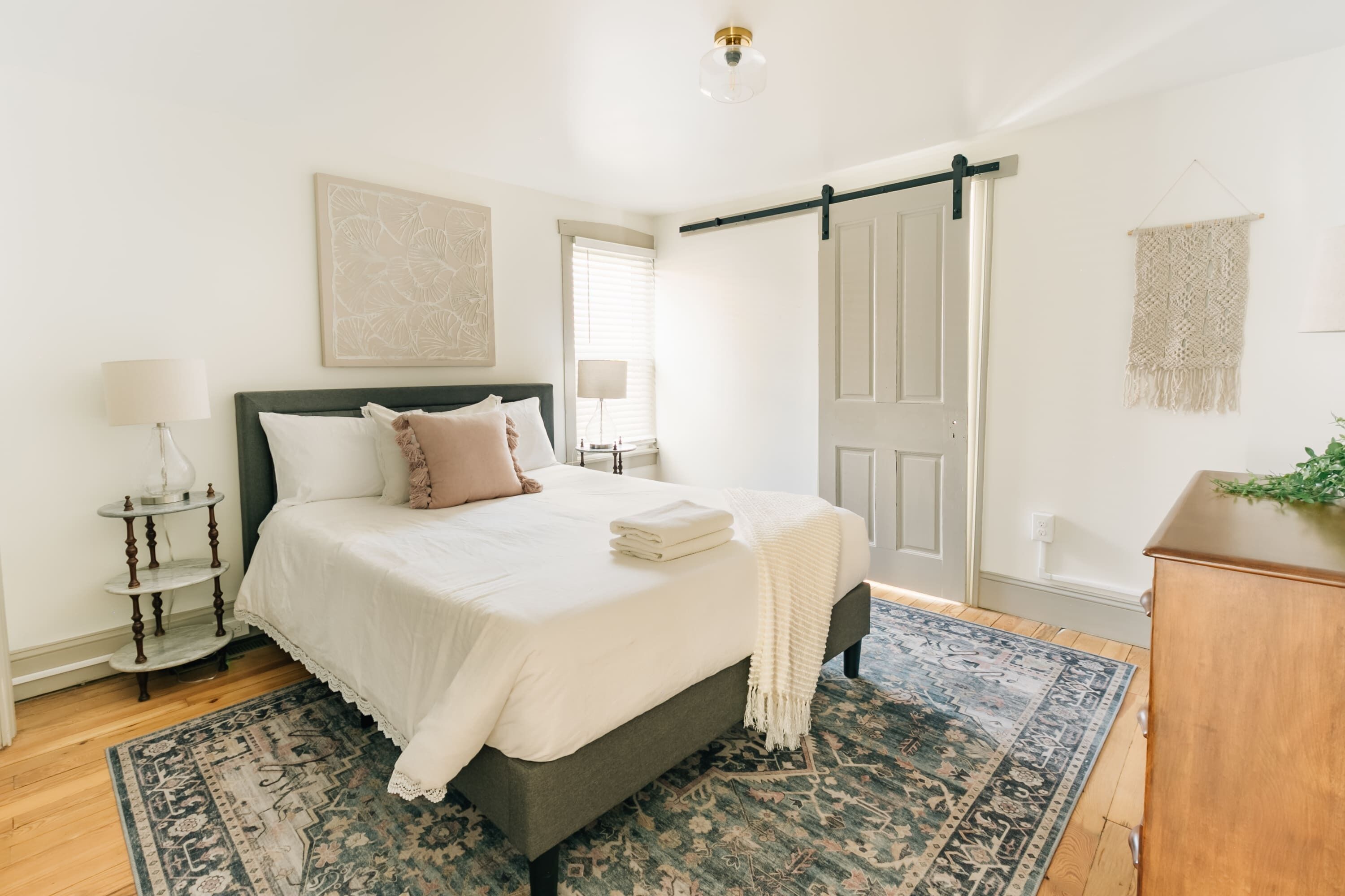Une chambre à coucher comprenant un lit, des tables de chevet, une commode, une porte et une décoration murale en macramé.