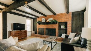 A living room with a brick fireplace, leather sofas, a wooden coffee table, and a TV on a wooden cabinet. - Quaint, Vintage Reno in Manheim (Manheim)