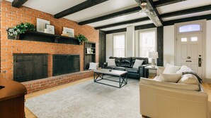 A living room with a brick fireplace, a black leather sofa, a white sofa, and a coffee table. - Quaint, Vintage Reno in Manheim (Manheim)