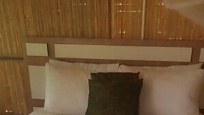 Una cama con una manta blanca y rosa, un almohadón verde y una alfombra rosa de pelo.