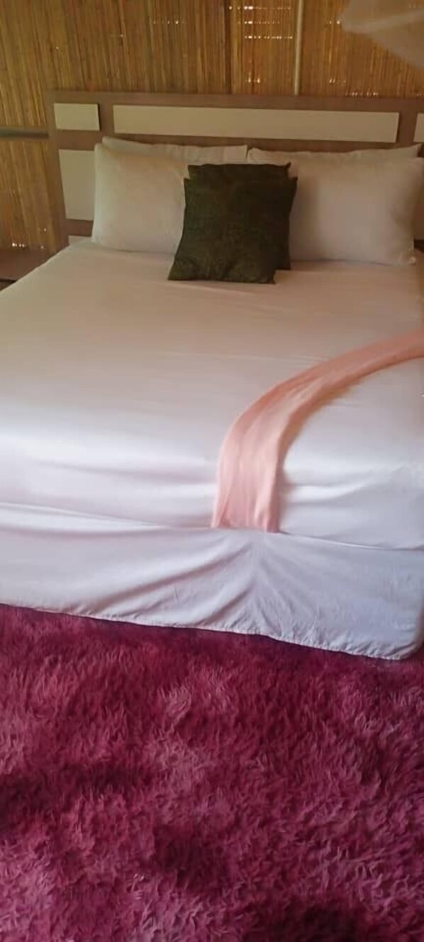 A bed with a white and pink blanket, a green pillow, and a pink furry rug.