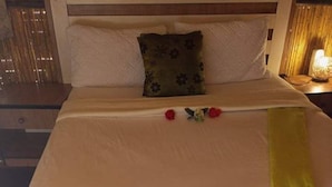 Una cama bien hecha con edredón blanco, una manta verde y dos flores rojas sobre el cubrecolchón.