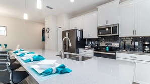 A modern kitchen with white cabinets, stainless steel appliances, and a central island with blue napkins. - Coastal! Value! Pool! Resort 6 mi 2 Disney! 4837 (Kissimmee)