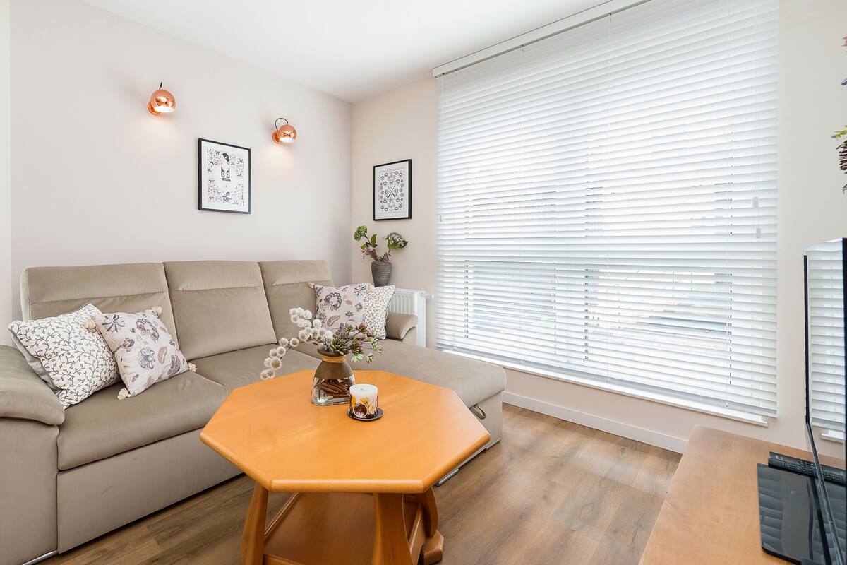 Una sala de estar con un sofá color crema, una mesa de centro de madera y dos lámparas de pared.