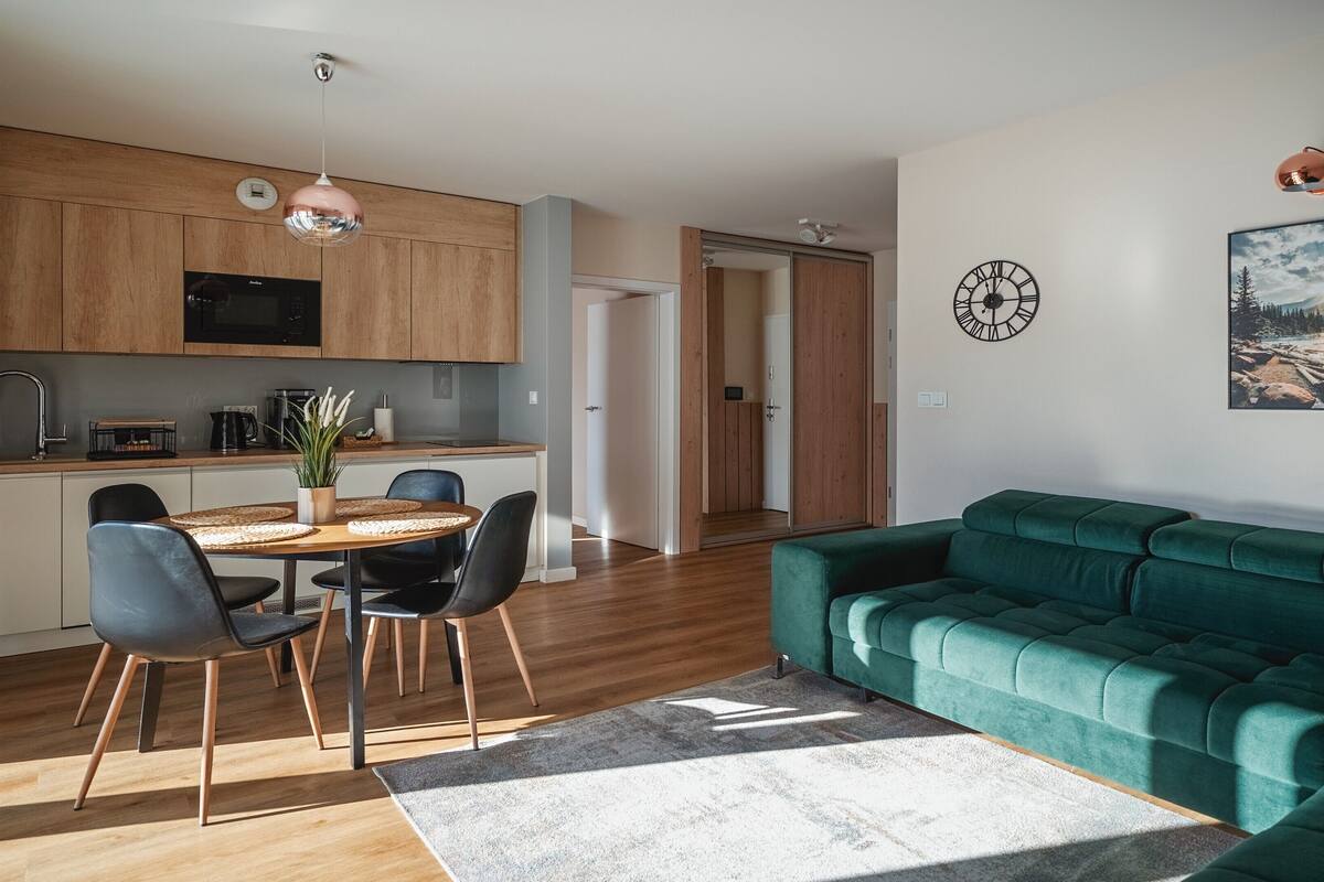 Una cocina moderna con armarios de madera, un comedor con una mesa redonda y sillas, y un sofá verde en una sala de estar.