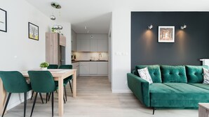 Una sala de estar moderna con un sofá verde, un comedor con una mesa y sillas de madera, y una cocina al fondo.