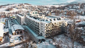 Un hotel de varios pisos con tejado nevado, situado en un pueblo cubierto de nieve y con montañas al fondo.