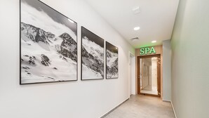 Un pasillo con tres fotografías enmarcadas de montañas en la pared, que conduce a la entrada de un spa con un letrero verde.
