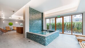 Uma área interna de piscina moderna com parede em mosaico, assentos de madeira e uma mesa de recepção.