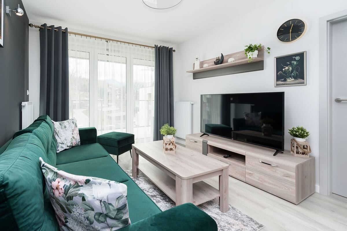 Una sala de estar moderna con un sofá verde, una mesa de centro de madera, un televisor de pantalla plana y una decoración minimalista.