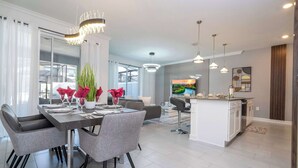 A modern dining area with a chandelier, grey upholstered chairs, and a central island with a sink. - Stunning 4 Bd w/ Pool @ Storey Lake Resort 2613 (Kissimmee)