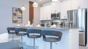 A modern kitchen with white cabinets, stainless steel appliances, and a central island with bar stools. - Stunning 4 Bd w/ Pool @ Storey Lake Resort 2613 (Kissimmee)