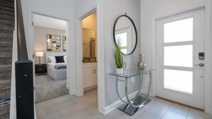 A modern interior with a staircase, a hallway leading to a bedroom, a glass console table with a mirror, and a door with a window. - Stunning 4 Bd w/ Pool @ Storey Lake Resort 2613 (Kissimmee)
