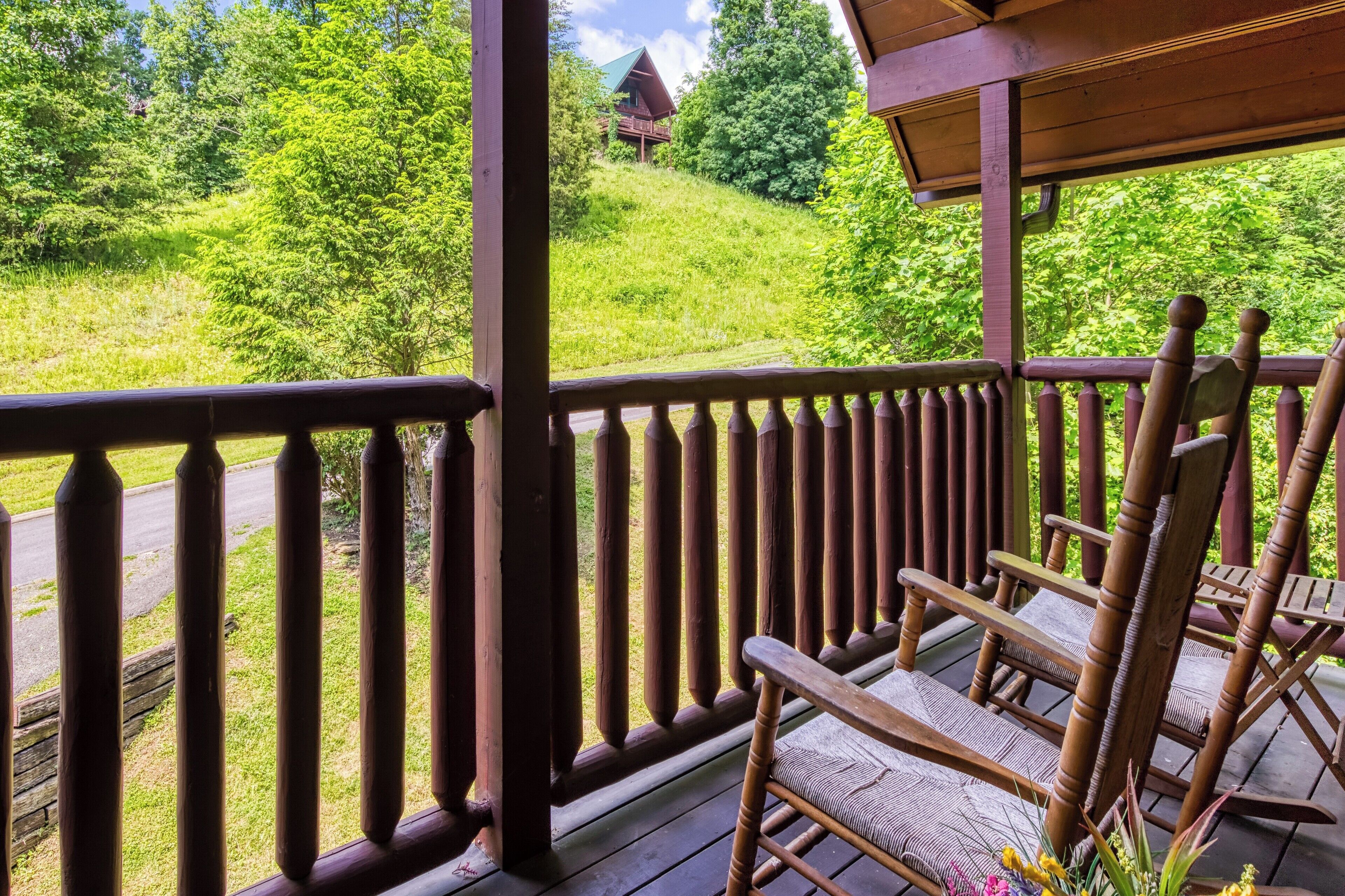 A wooden deck with a railing, a rocking chair, and a view of a green landscape with trees and a building in the distance.
