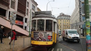A tram with a Coca-Cola advertisement on its front, traveling on a track in an urban area with buildings and a parked van. - Apartamento 73 com Terraço (Lisbon)