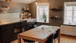 A modern kitchen with a wooden dining table, black chairs, and a large window with a plant.
