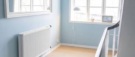 Une pièce aux murs bleu clair, avec un radiateur blanc, une grande fenêtre à cadre blanc et un plafond blanc.