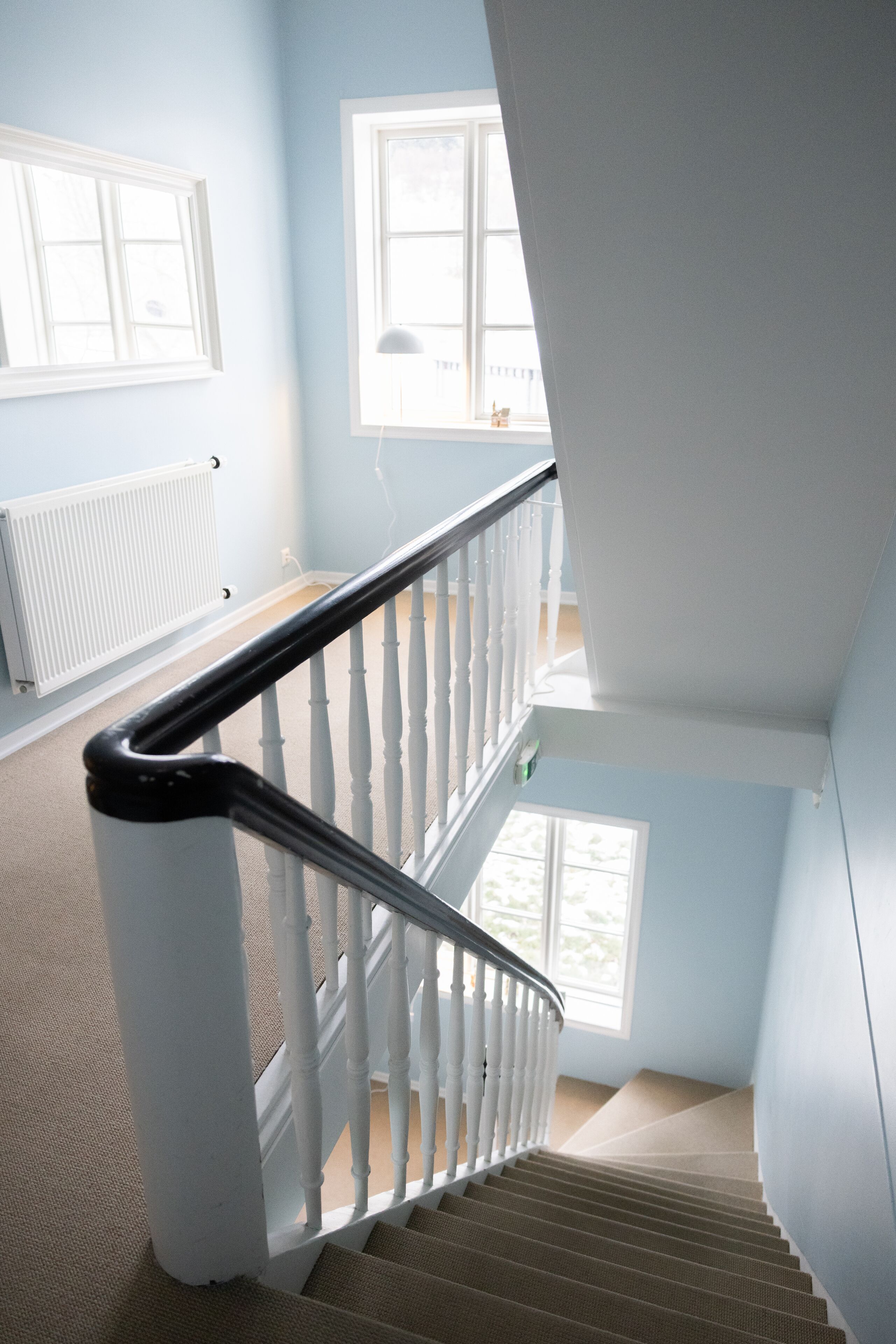 A staircase with white balusters and a black handrail, leading to a landing with a window and a radiator.