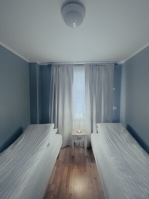 A hotel room with two single beds, a small desk, and a window with curtains.