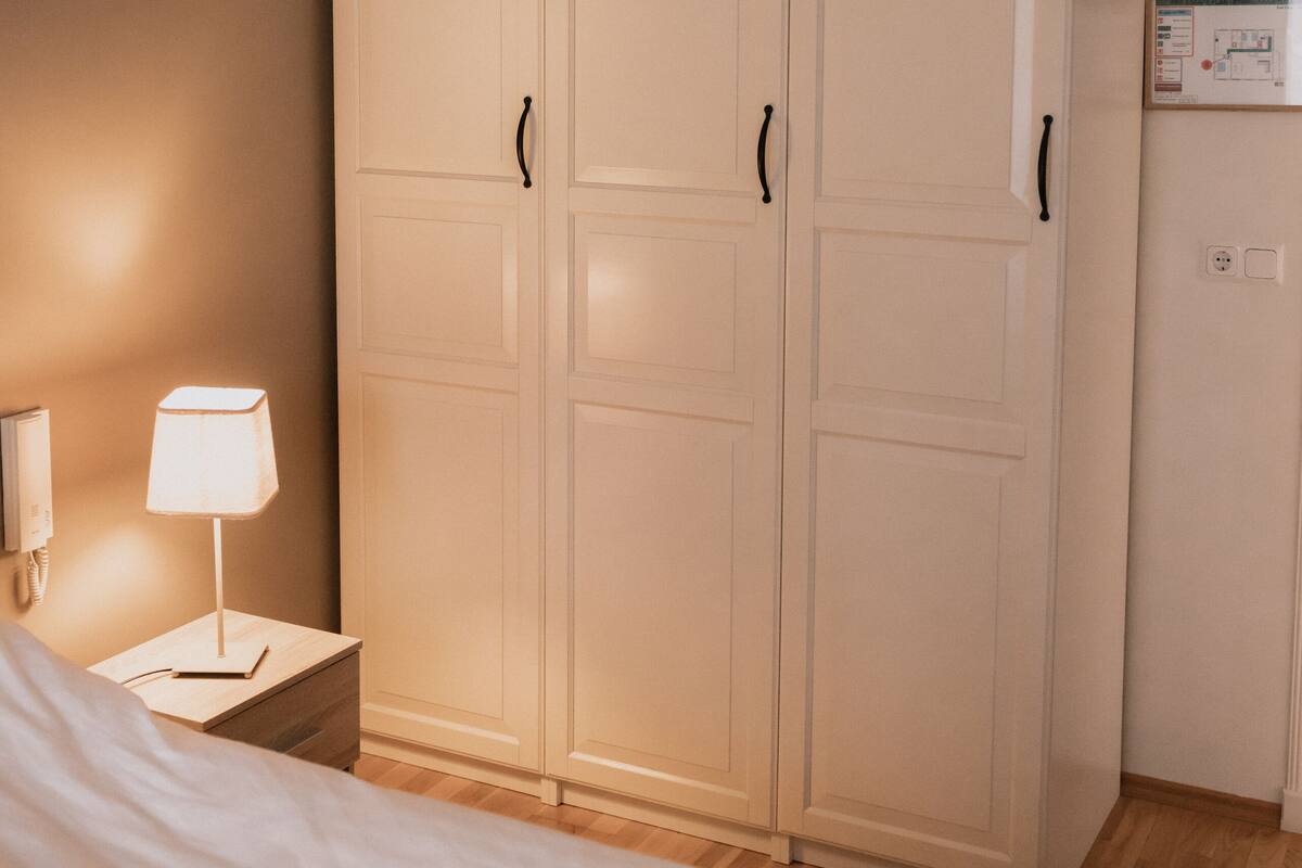 A bedroom with a bed, a nightstand, a lamp, and a wardrobe.