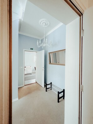 A hallway with a chandelier, a mirror, and a bench.