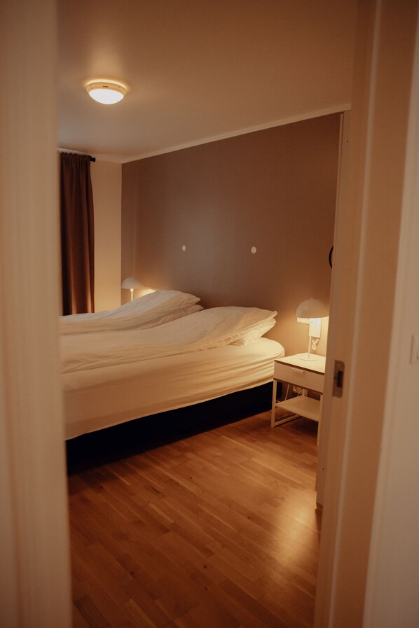 Un dormitorio con una cama, mesitas de noche, una lámpara de techo y suelo de madera.