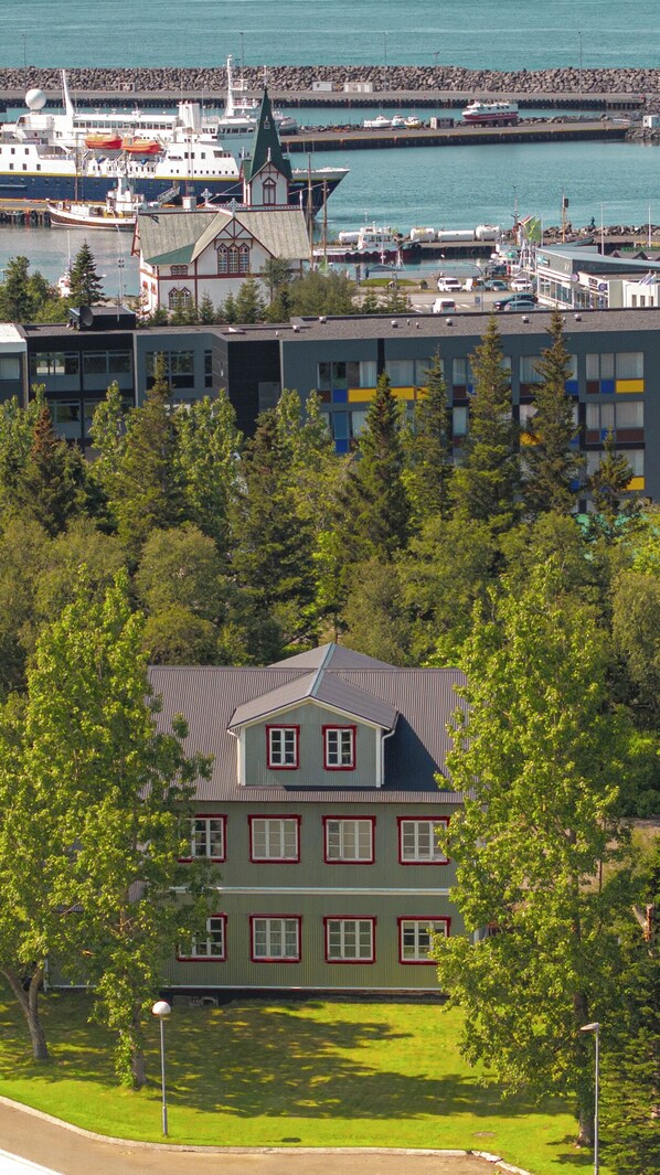 A large building with a green roof and multiple windows, surrounded by trees and a body of water with boats.
