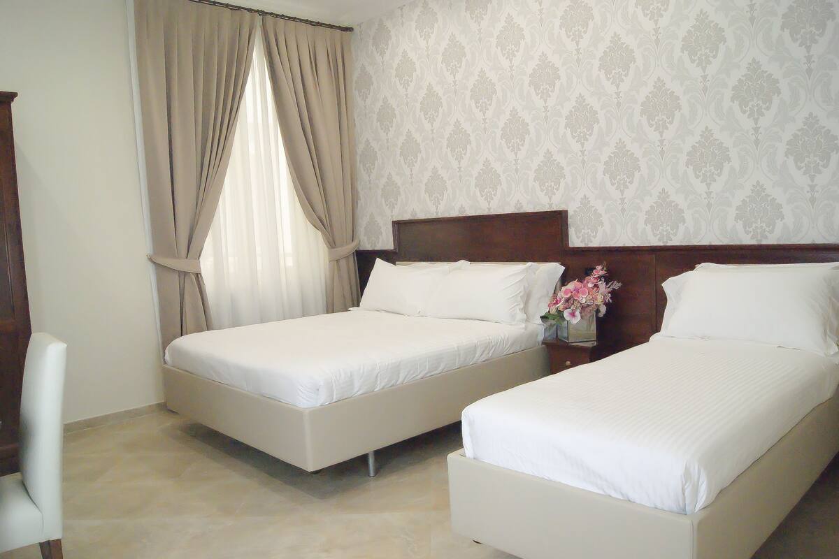 Habitación de hotel con dos camas, cabecera de madera, una silla y una ventana con cortinas.