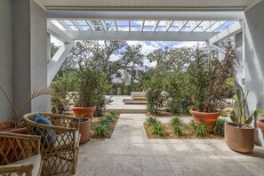 Een terras buiten met een pergola, plantenpotten en een zithoek.