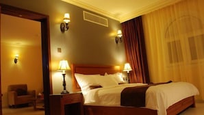 Ein Hotelzimmer mit einem hölzernen Bett, zwei Nachttischlampen, einem Nachttisch, einem Sessel und einem Fenster mit Vorhängen.