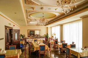 Un comedor formal con varias mesas y sillas, un candelabro y un espejo grande en la pared.