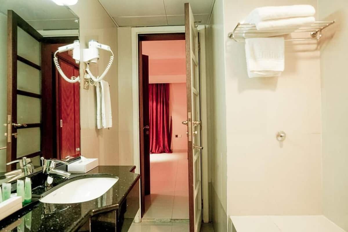 Une salle de bain d’hôtel avec un lavabo noir, un miroir, un sèche-cheveux et un porte-serviettes.