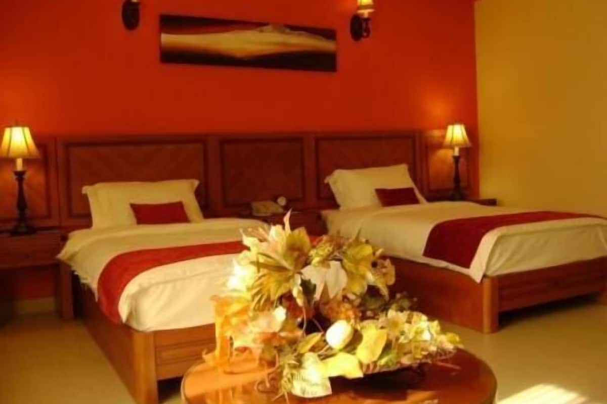 Une chambre d’hôtel avec deux lits, une tête de lit en bois, une table ronde agrémentée d’un centre de table floral et deux lampes de chevet.
