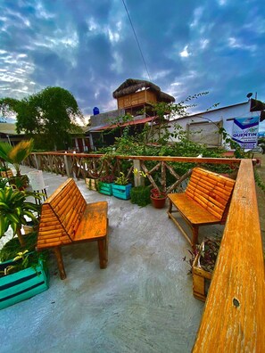 A patio area with wooden benches and potted plants. - Hostal Machalilla (Puerto Lopez)