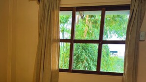 A bed with a patterned blanket, a window with a view of greenery, and a curtain.