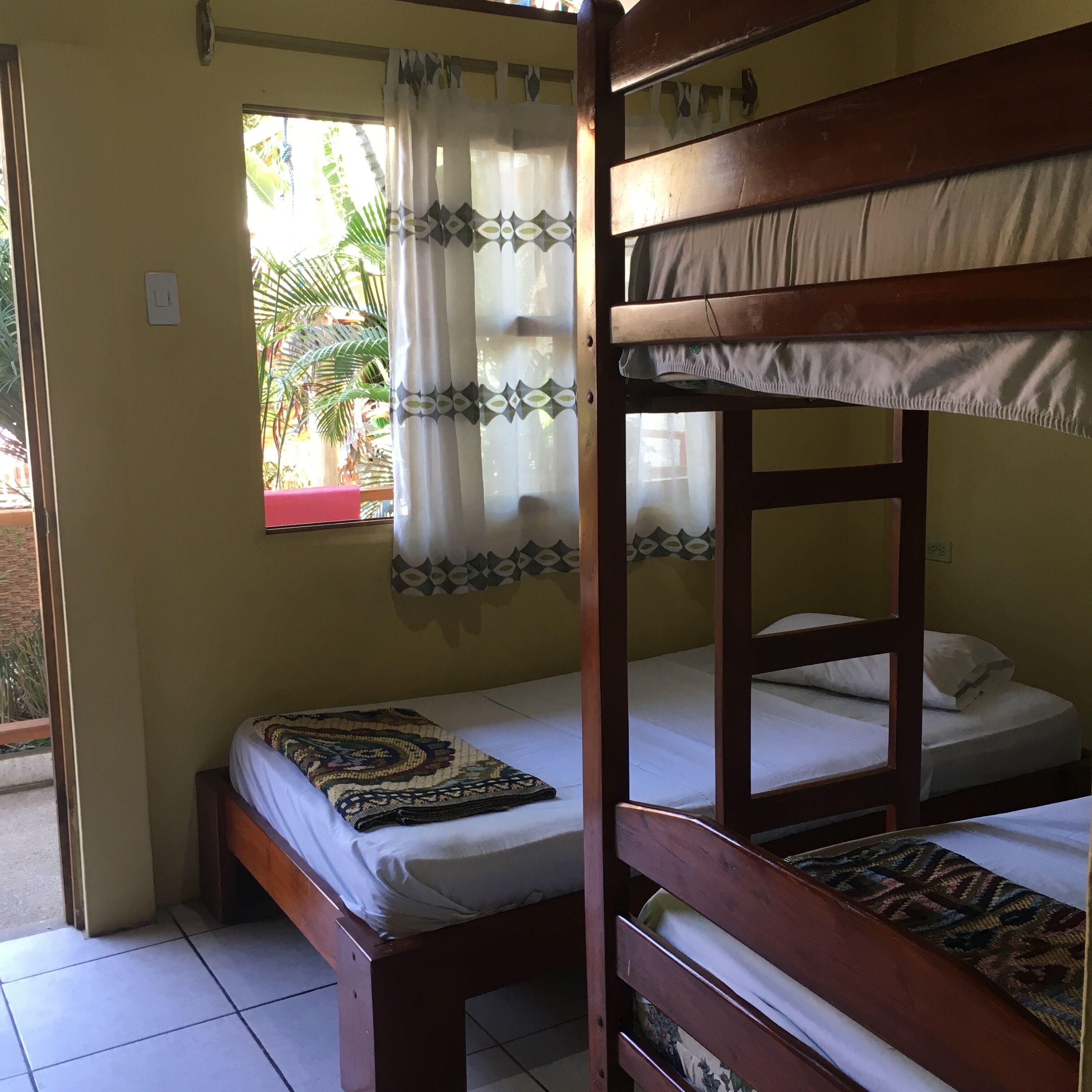 A room with two bunk beds, a window with a curtain, and a small table with a patterned tablecloth.