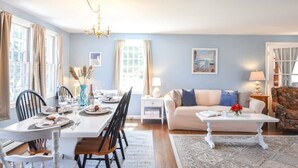 A dining area with a white table set for four, a sofa, and a patterned rug. - Sleeps 8, Minutes to Nauset Beach! (Orleans)