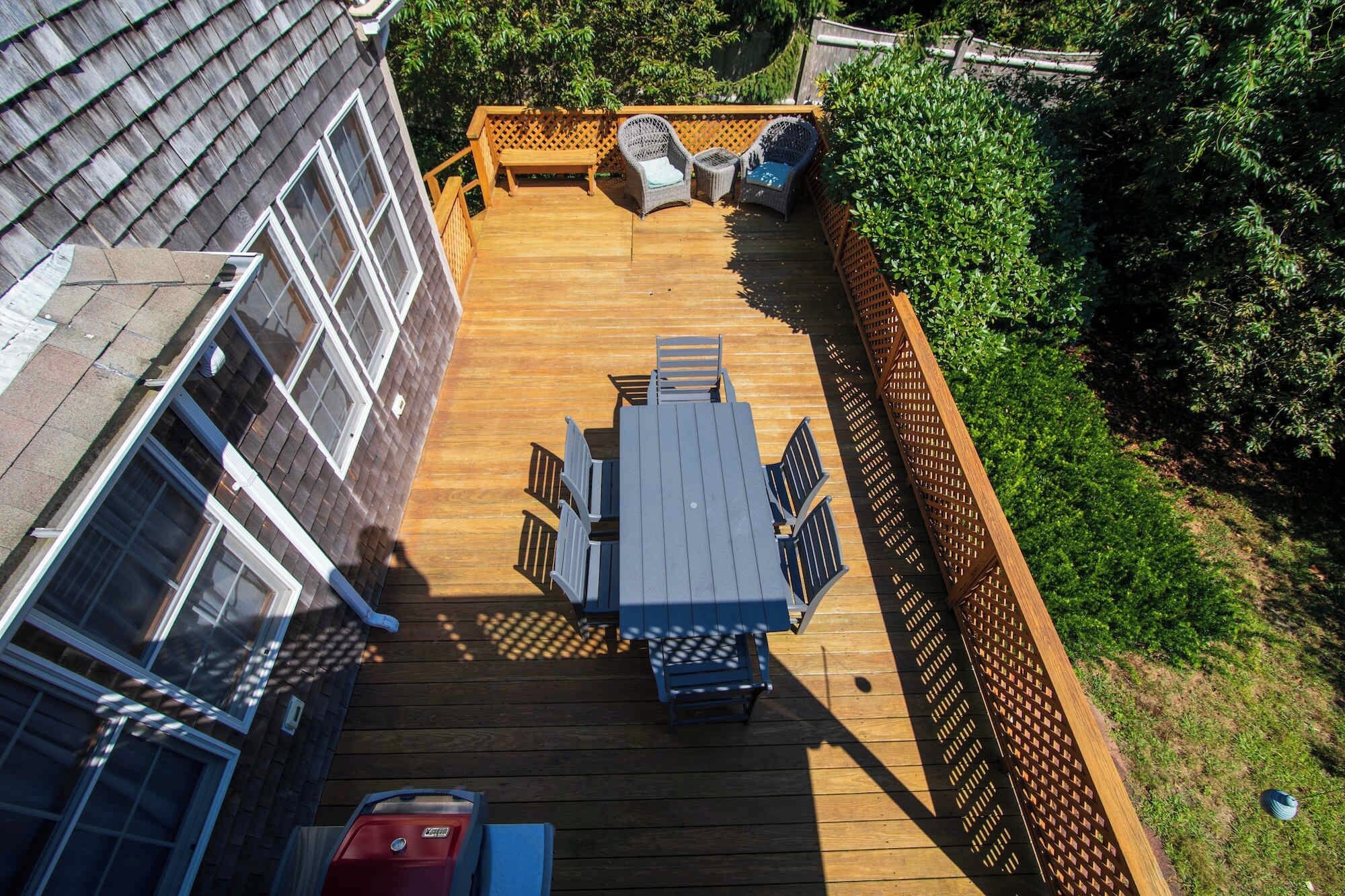 A deck with a table and chairs, surrounded by a wooden fence and greenery.