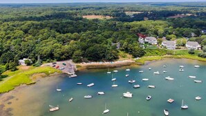 Vista aérea de una zona costera con varios barcos amarrados en una bahía tranquila, rodeada de vegetación exuberante y edificios residenciales.
