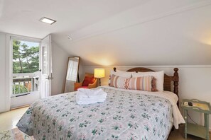A bedroom with a bed, a nightstand, a lamp, a mirror, and a door leading to an outdoor area. - Walk to Private Beach on Buck's Pond! (Harwich)