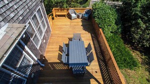 Una terraza con mesa y sillas, rodeada por una valla de madera y follaje.