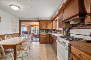 A kitchen with wooden cabinets, a stove, and a dining area with a table and chairs. - Walk to Private Beach on Buck's Pond! (Harwich)