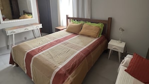 A bedroom with a bed, a bedside table, a lamp, a dresser, a mirror, and a window with curtains.