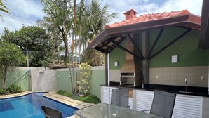 A backyard with a swimming pool, a glass table with chairs, and an outdoor kitchen area.