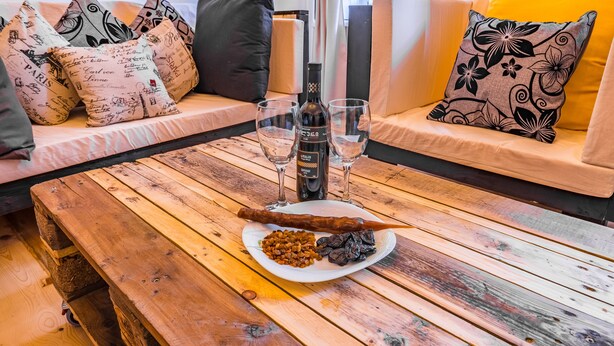 Ein Holztisch mit einer Weinflasche, zwei Gläsern, einem Teller mit Essen und einer hölzernen Bank.